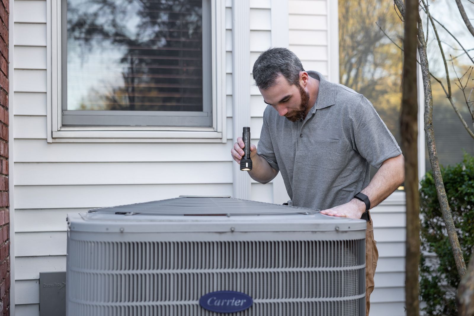 A Climate Control AC technician inspecting a residential air-conditioning condenser unit beside a home in Hurricane, Utah