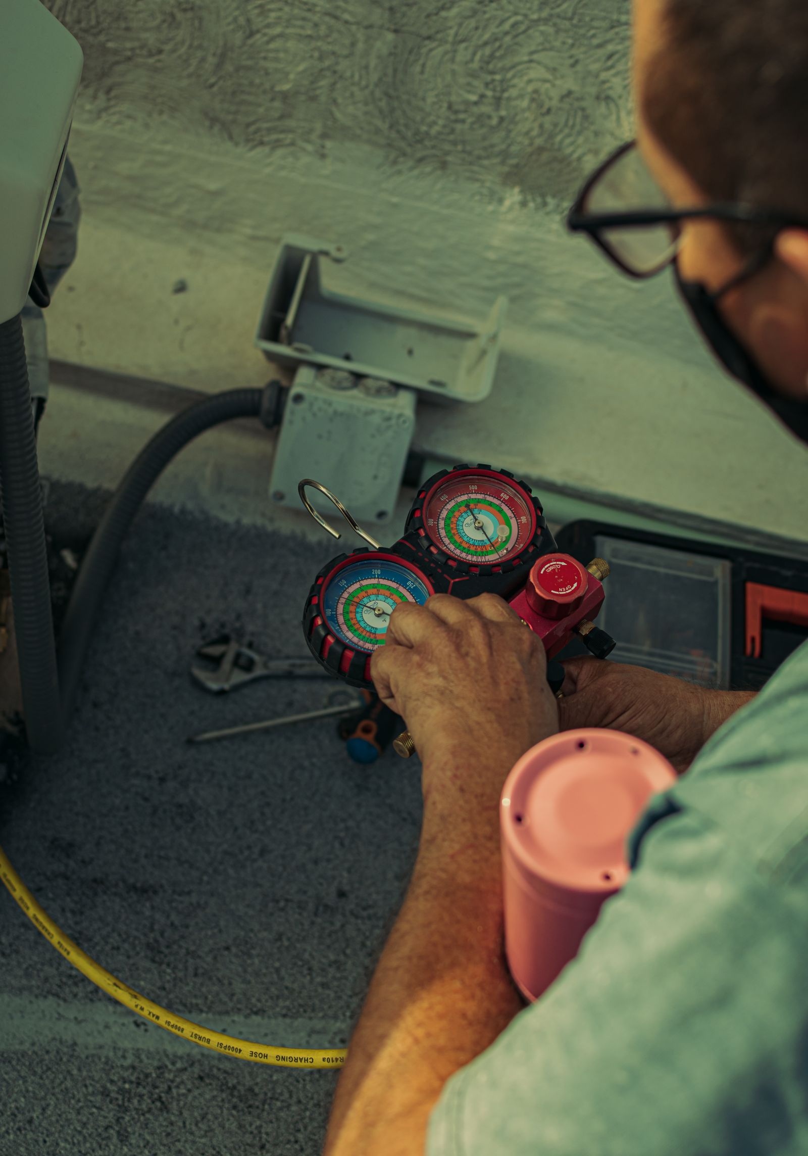 Close-up of refrigerant manifold gauges in a Climate Control AC technician's hands during an air-conditioning service call